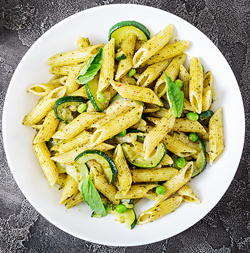 Penne pasta with  pesto sauce, zucchini, green peas and basil. Italian food. Top view. Flat lay.