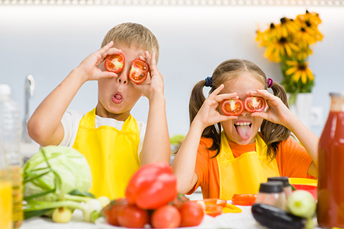 Happy kids having fun with food vegetables at kitchen holds toma