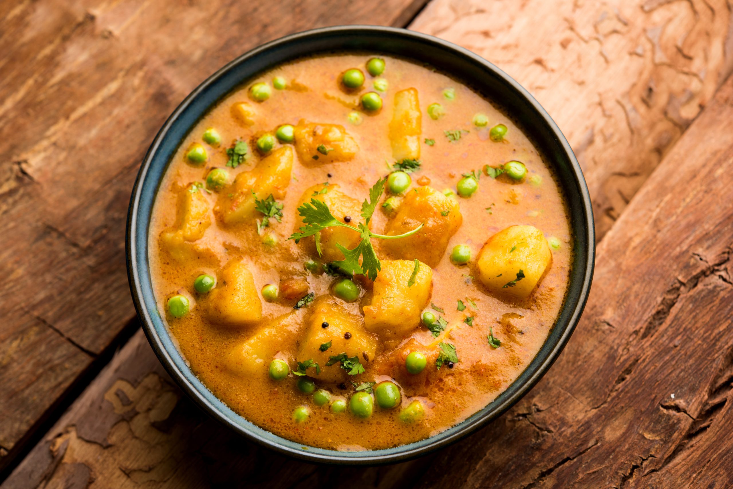 Indian Aloo Mutter curry - Potato and Peas immersed in an Onion Tomato Gravy and garnished with coriander leaves. Served in a Karahi/kadhai or pan or bowl. selective focus