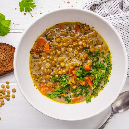 Homemade vegan lentil soup with vegetables and cilantro, white wooden background, top view. Indian vegetarian cuisine.