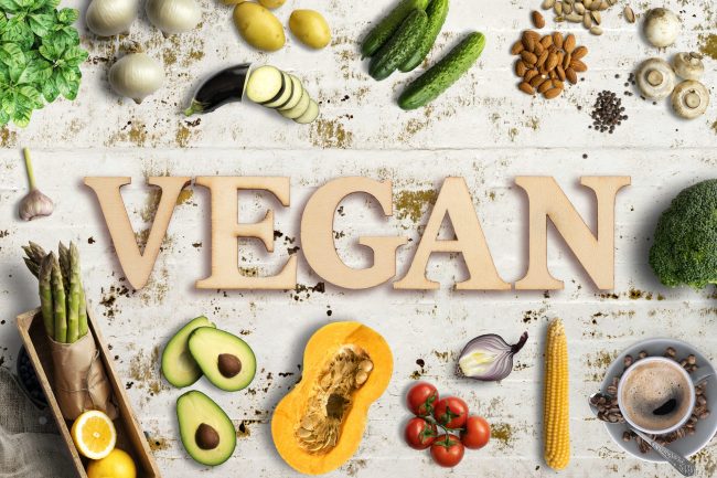 Word “vegan” in wooden letters with many cooking ingredients