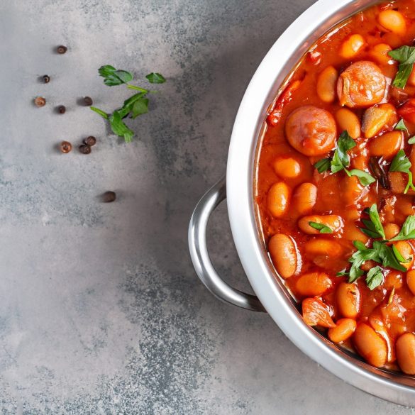 hearty beans stew with sausages, herbs and spices in tomato sauce in a metal casserole on a concrete table, fasolka po bretonsku, polish cuisine, view from above, flatllay, copy space