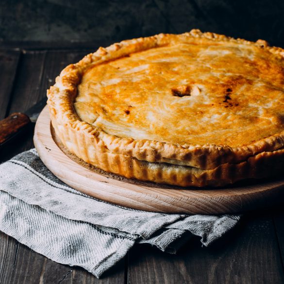 Fresh Whole Meat pie on the wooden board on table background. Pie with cabbage and minced beef