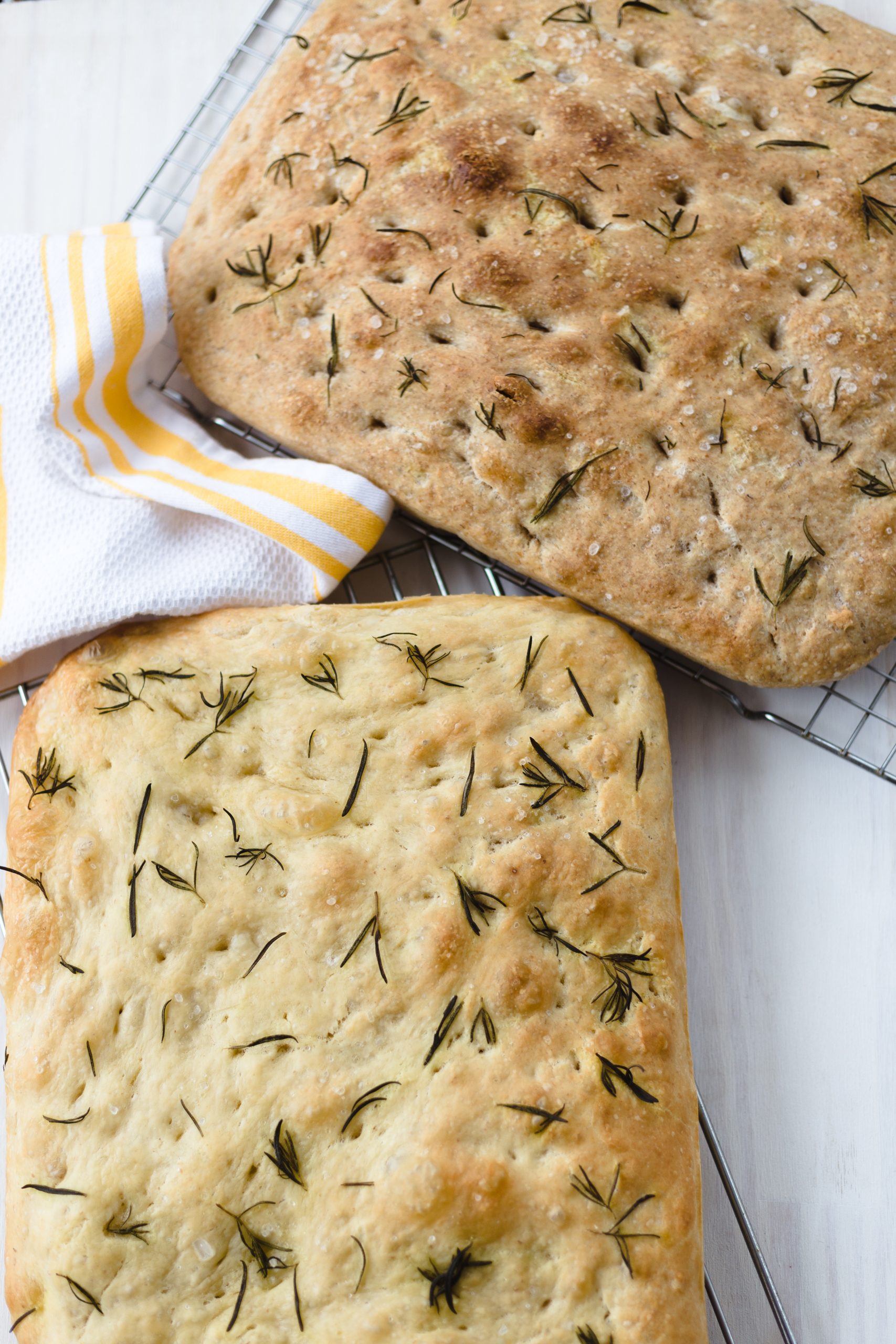 rosemary focaccia on a white surface and yellow kitchen towel