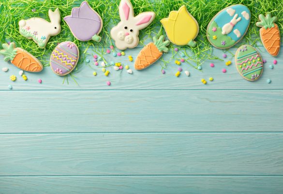 Easter cookies, bunnies and eggs with colorful sprinkles on decorative grass top view on light blue background