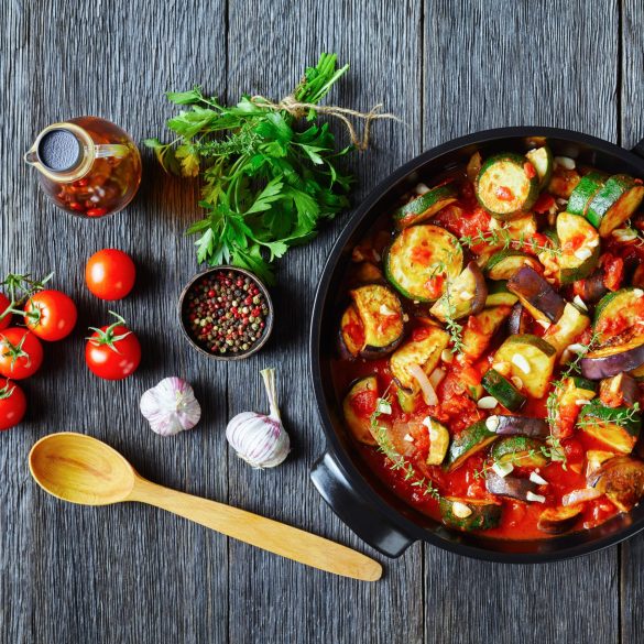 vegetable stew, eggplant, onion, zucchini with tomato sauce, garlic and herbs in a baking dish on a wooden table with ingredients, landscape view from above, close-up, flat lay, free space