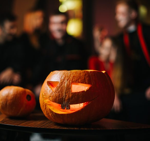 Halloween carved pumpkin on the table at the cafe. Against the background of a group of friends celebrating on the eve of Saints' Day. There's a candle burning inside the pumpkin