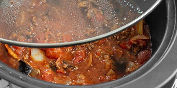 Bolognese sauce cooking in a slow cooker with glass lid lifted o