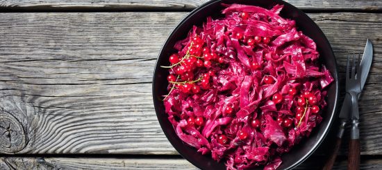 Danish Red Cabbage cooked with vinegar and red currant juice served with berries in a black bowl on a rustic wooden table, horizontal view from above, flatlay, copy space