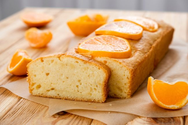 Loaf of gluten free tangerine cake with pieces of mandarin on rustic wooden background. Close up slice of citrus pie by classic recipe. Healthy nutrition, homemade vegan dessert.