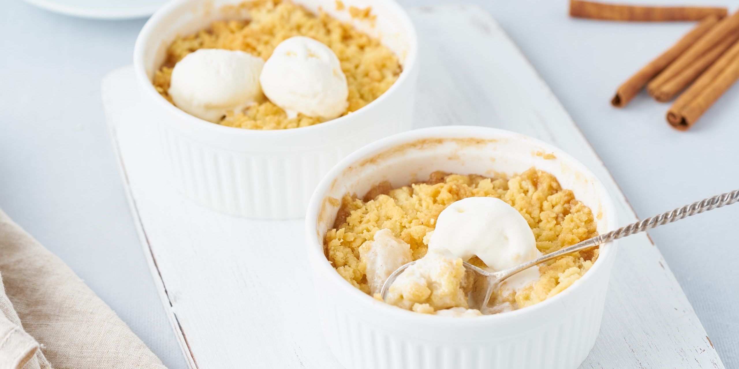 Apple crumble with ice cream, spoon with streusel. Morning breakfast on light gray table. Side view, close up