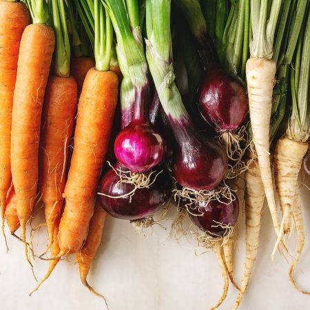 Variety of root garden vegetables carrot, purple onion, beetroot, parsnip with tops over white marble background. Top view, space