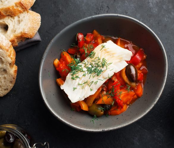 Delicious fish stew in paprika, tomatoes and white wine. Cod fillet white sea fish with organic vegetables, olives, onions, carrots, tomatoes, capsicum in a baking dish for lunch. Top view