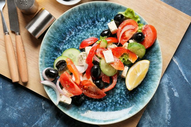 Plate of fresh Greek salad on color background