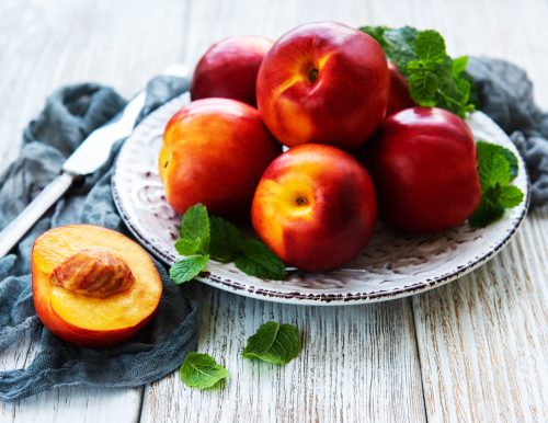 Plate with fresh nectarines on a white wooden table