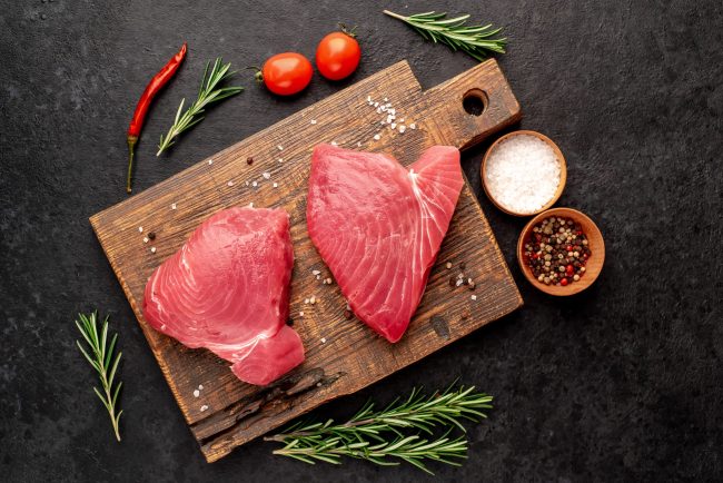 Fresh raw tuna steaks with rosemary and spices on a stone backgr