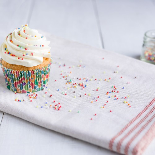 Sprinkled vanilla cupcake with white chocolate butter cream frosting, on the kitchen towel on a white background.