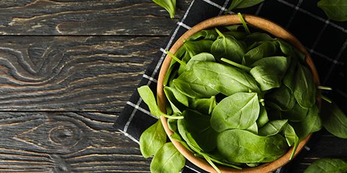 Wooden bowl with spinach and napkin on wooden background