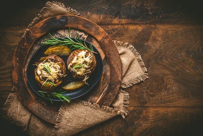 Two baked potatoes with mushrooms, sour cream and cheese on a ru