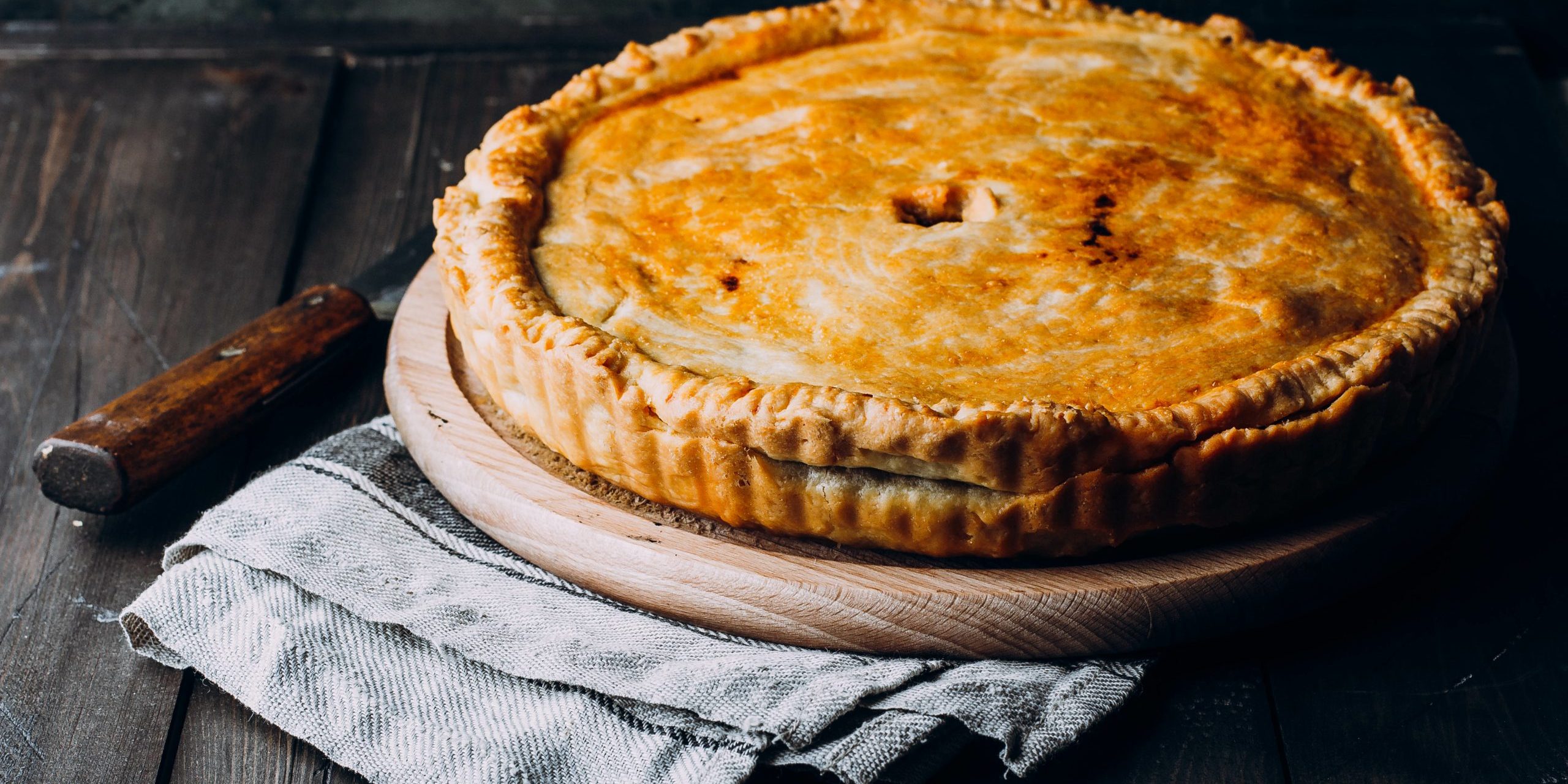 Fresh Whole Meat pie on the wooden board on table background. Pie with cabbage and minced beef