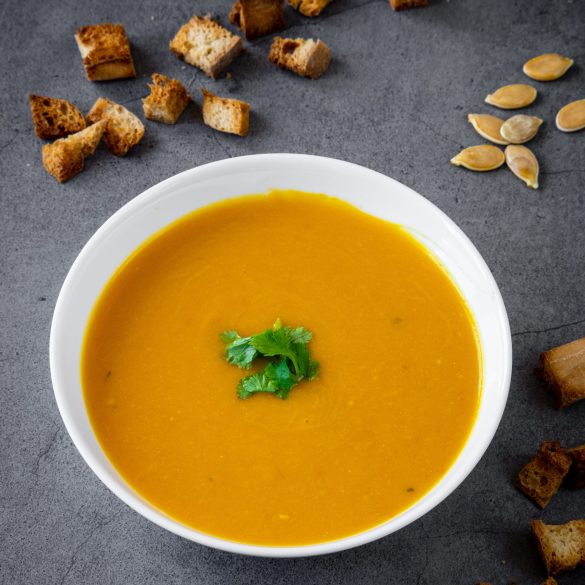 Pumpkin soup with coriander in a white bowl with croutons and pumpkin seeds in the background. Seasonal autumn / winter food, healthy and fresh