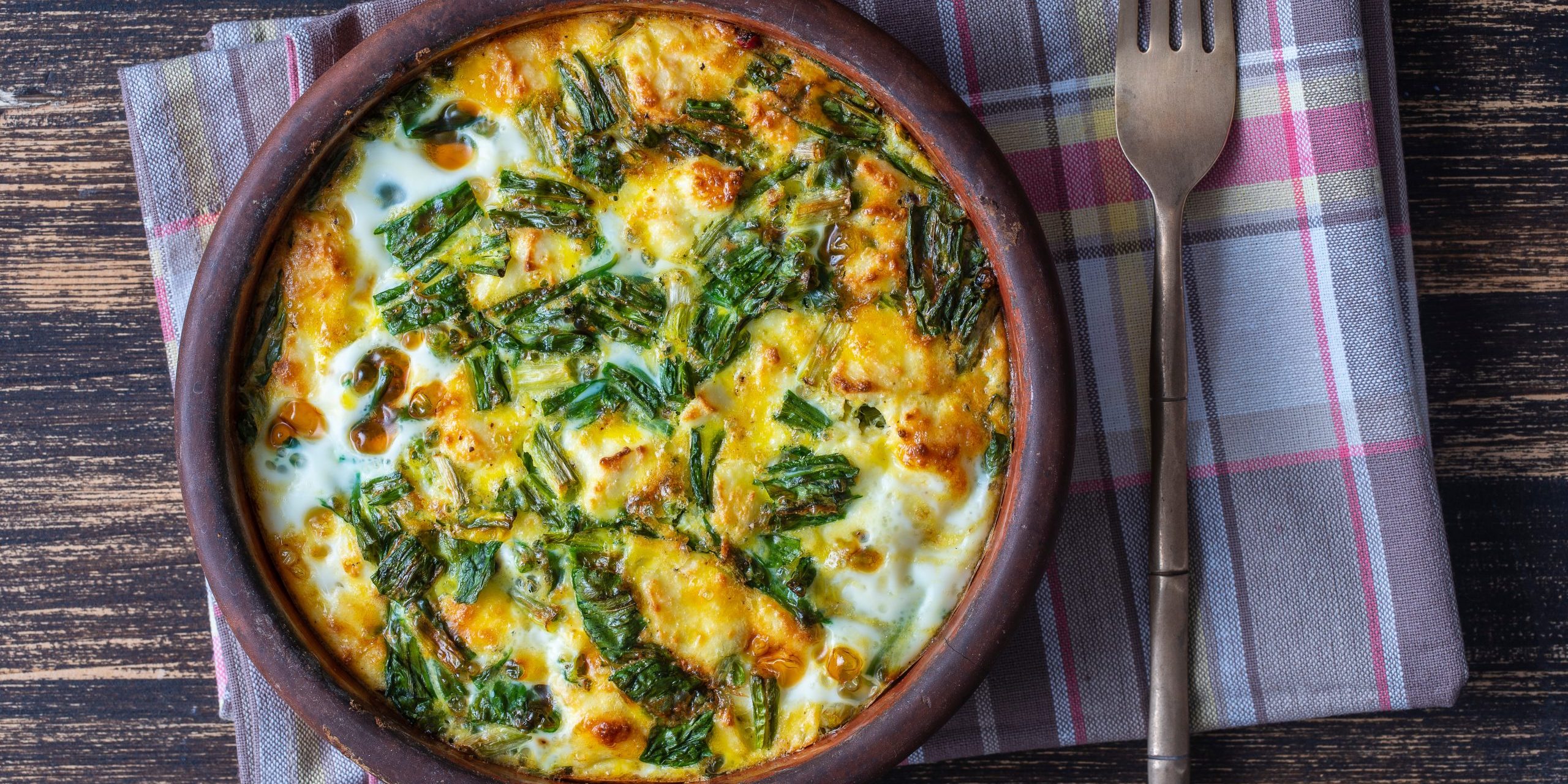 Ceramic bowl with vegetable frittata, simple vegetarian food. Frittata with egg, pepper, onion, cheese and green wild garlic leaves on table