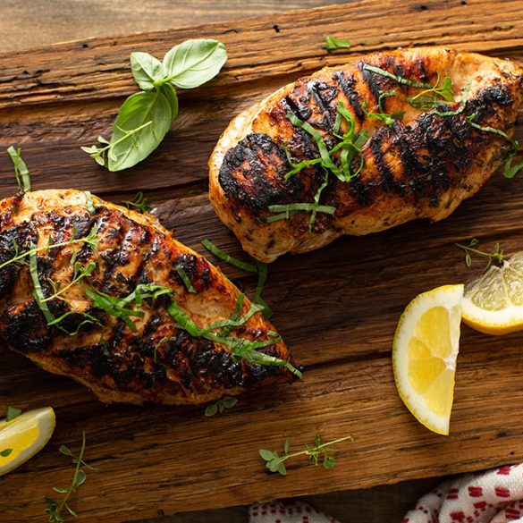 Balsamic grilled chicken breast with fresh herbs on a rustic wooden board