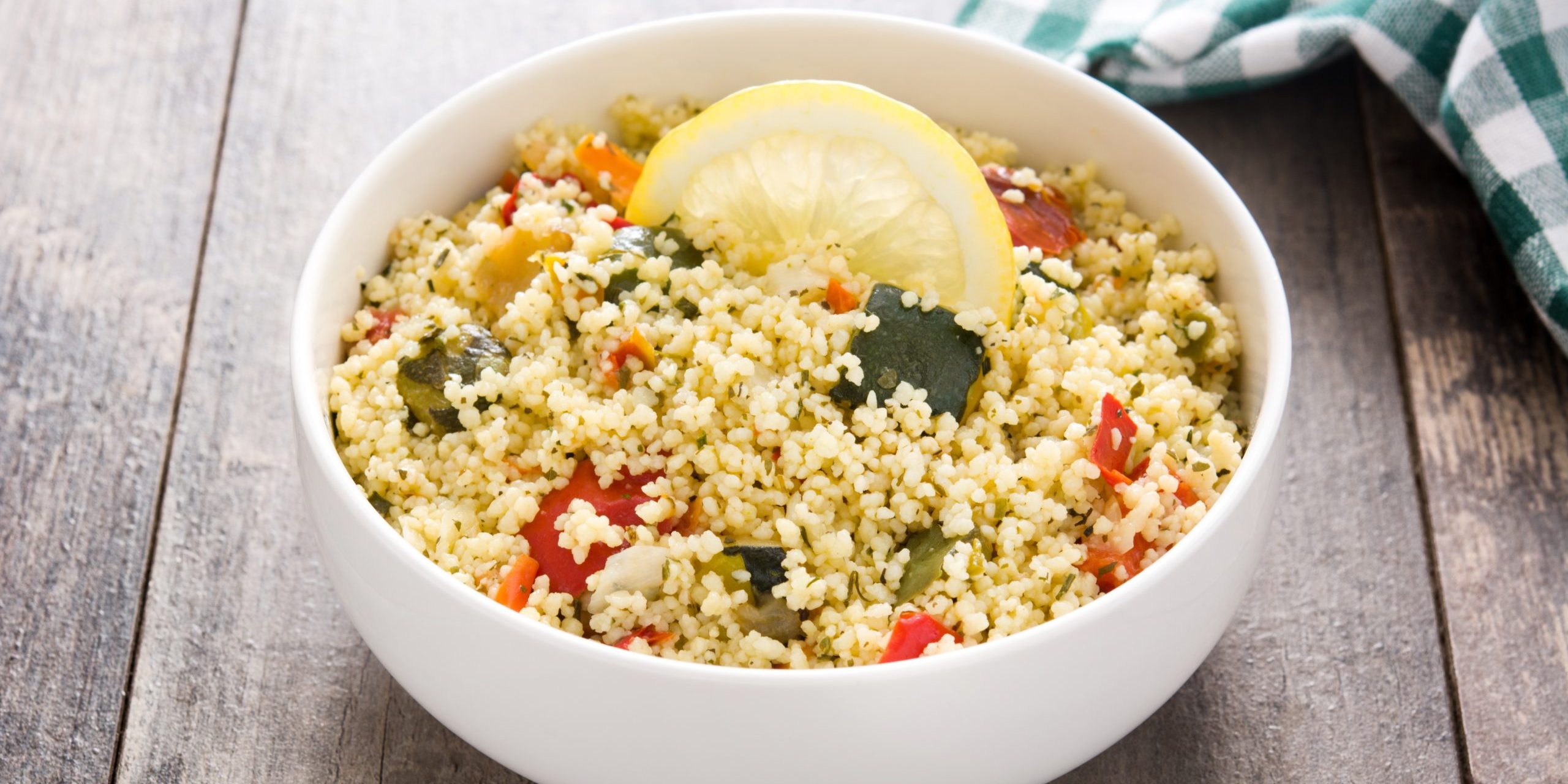 Couscous with vegetables in bowl on wooden table.