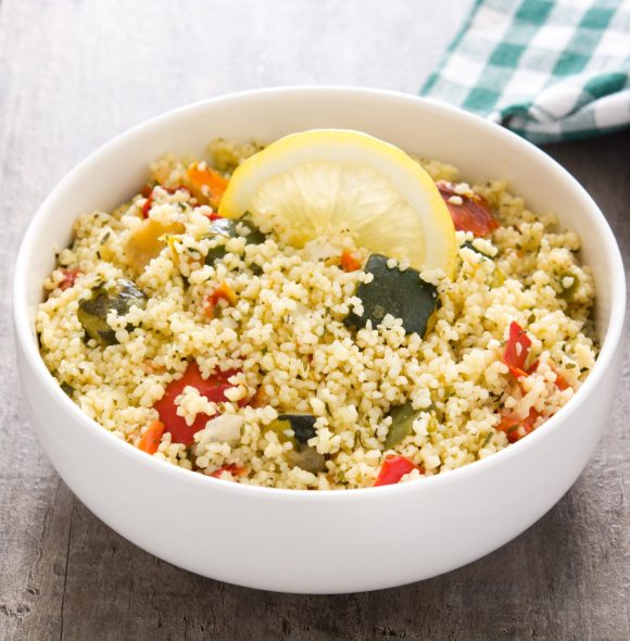 Couscous with vegetables in bowl on wooden table.