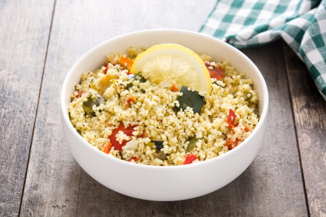 Couscous with vegetables in bowl on wooden table.
