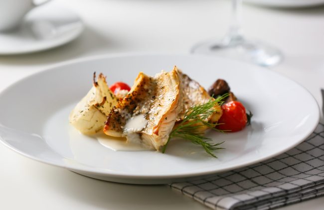 Plate with tasty baked cod fillet, vegetables and sauce on table