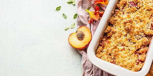 Yummy peach crumble dessert in baking pan on light background ,