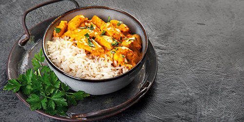 Indian butter chicken curry with basmati rice on dark background