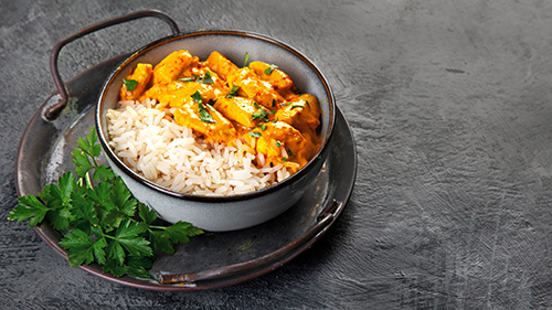 Indian butter chicken curry with basmati rice on dark background