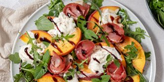 Healthy summer salad with peach, burrata, arugula and jamon
