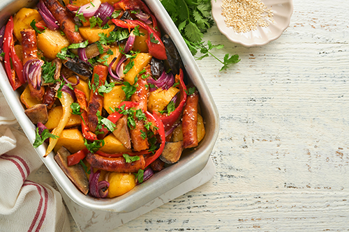 Baked sausage and vegetables, peppers, zucchini, tomatoes, red onion and eggplant with sesame and cilantro served hot from oven on baking tray. Traditional lunch dish BBQ. Sausage jersey tray bake.