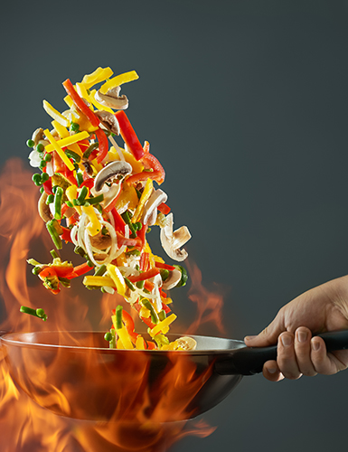 Frying pan wok with vegetables in the air on fire. Vegetables wok – peppers, onions, peas, mushrooms, beans, broccoli, zucchini. Asian food. Chinese food. The effect of levitation