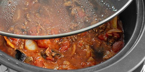 Bolognese sauce cooking in a slow cooker with glass lid lifted o