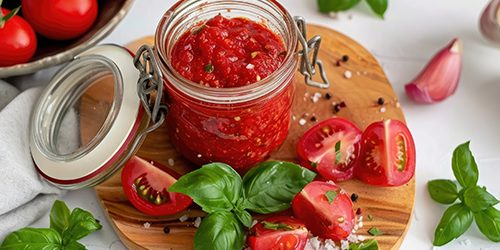Homemade tomato relish in a glass jar, surrounded by fresh ingredients